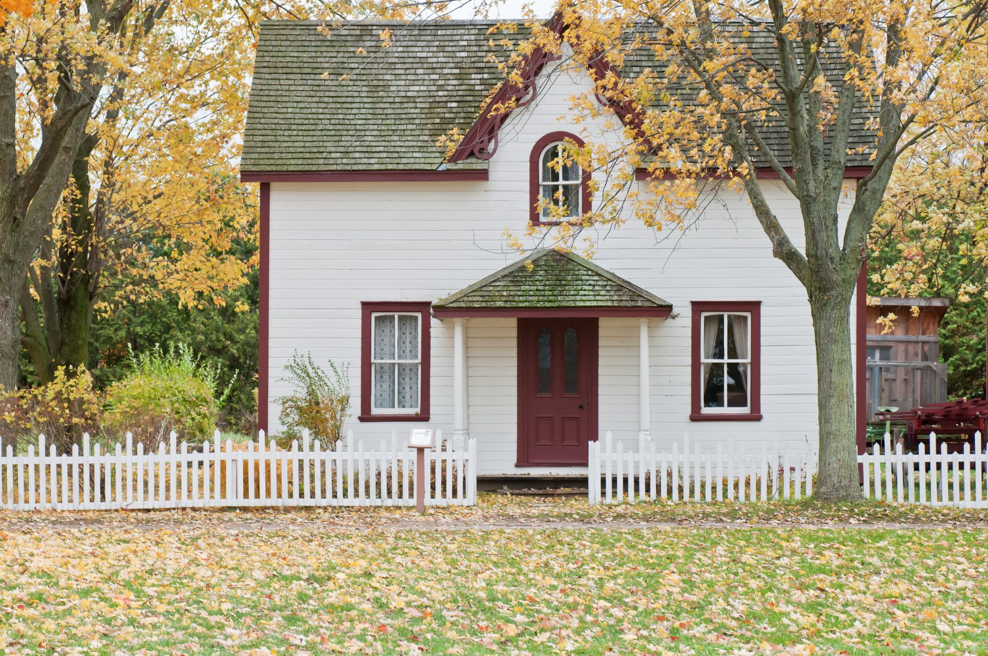Farmhouse framed by a white picket fence in autumn